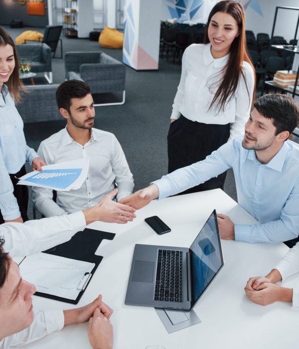 Handshake for success deal. Top view of office workers in classic wear sitting near the table using laptop and documents.