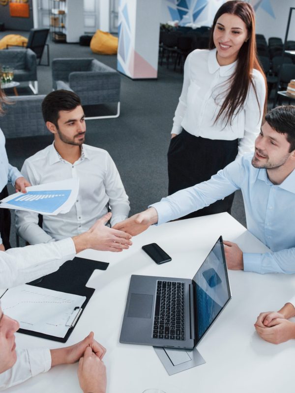Handshake for success deal. Top view of office workers in classic wear sitting near the table using laptop and documents.